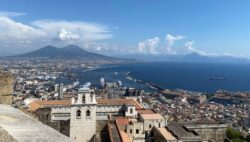 Overview of Naples, Italy, with buildings in the foreground and mountains and the sea in the background.